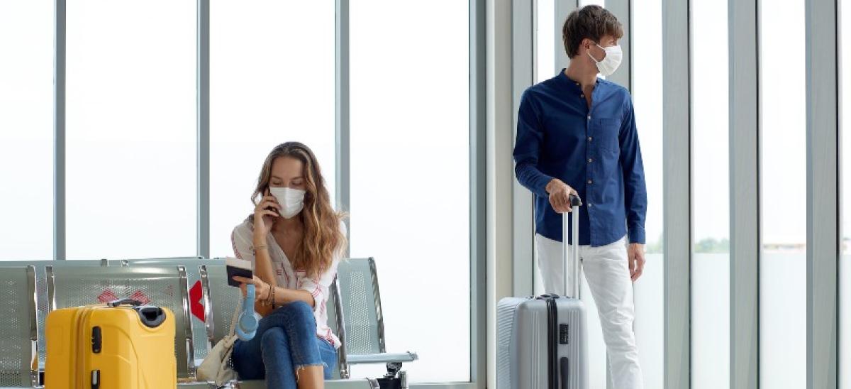 Dos viajeros con mascarilla en la zona de embarque de un aeropuerto.